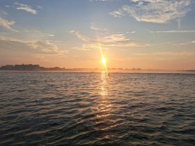 A stunning sunset casts a golden glow over the water, creating a picturesque coastal scene perfect for evening boat trips.