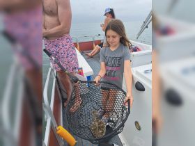 A young girl proudly holds a fishing net with her catch while enjoying a family fishing trip on a boat — a memorable moment on the water.