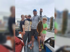 A joyful family celebrates their fishing catch, showcasing a flounder on board — a memorable moment of fishing fun together.