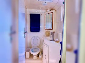 A clean and functional bathroom inside a boat, featuring a toilet, sink, and storage, perfect for onboard convenience.