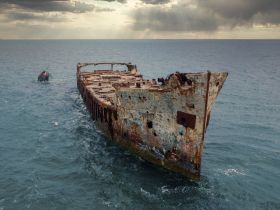 An aerial view of a rusted shipwreck emerging from the ocean, showcasing the haunting beauty of maritime history.
