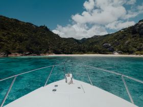 A stunning view from the bow of a boat cruising towards a secluded beach, surrounded by lush greenery and crystal-clear waters, perfect for exploring hidden gems.
