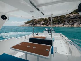 Interior view of a spacious boat cabin featuring comfortable seating and a scenic backdrop of turquoise waters and rocky shores, perfect for relaxing on a day out at sea.