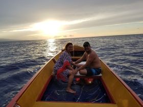 A couple enjoys a serene moment on a boat at sunset, surrounded by the vast ocean — a perfect setting for romantic getaways or sunset cruises.