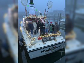 A festive group celebrates Christmas aboard a decorated boat, complete with lights and a snowman, creating a joyful atmosphere for holiday gatherings on the water.