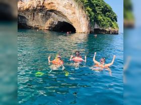 A joyful group of snorkelers celebrates in the clear waters near a stunning cave, showcasing the excitement of underwater adventures.
