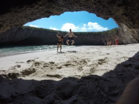 A lively scene at the beach with friends jumping for joy under a natural rock formation, capturing the essence of adventure and fun in a picturesque setting.