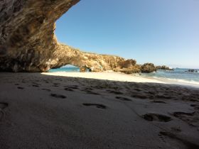 A scenic view of a beach with a group of people exploring the coastline, framed by natural rock formations — a perfect destination for beach lovers and adventure seekers.