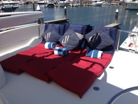 Cozy lounge area on a boat featuring plush cushions and rolled towels, perfect for relaxing in the sun while enjoying the marina views.