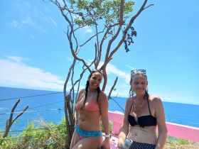 Two women enjoy a sunny day by the ocean, capturing a moment of fun and relaxation against a stunning coastal backdrop.