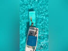 Two friends enjoy a sunny day on a floating mat in crystal-clear turquoise waters, with a boat nearby — a perfect scene for summer fun and relaxation.