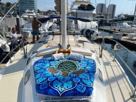 Two individuals stand on the deck of a sailboat, showcasing a colorful blanket and seating area, perfect for relaxation and enjoyment while docked.