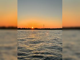 A stunning sunset over the water, with a silhouette of a cross in the background, creating a picturesque scene perfect for evening boat cruises.