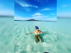 A woman enjoys a refreshing swim in the crystal-clear waters of a tropical paradise, with a stunning island backdrop — perfect for beach lovers and adventure seekers.