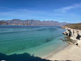 A stunning view of a tranquil coastline with crystal-clear waters and majestic mountains in the background, perfect for nature lovers and scenic boat trips.