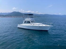 A sleek yacht named 'Mazuenda' cruising through clear waters, set against a backdrop of mountains and coastal scenery.