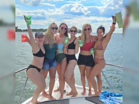 A lively group of friends celebrates on the bow of a boat, raising their cocktails against a scenic waterfront backdrop — perfect for summer parties and fun on the water.