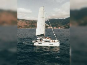 A lively group enjoys a sailing adventure aboard a catamaran, surrounded by stunning coastal scenery — perfect for group outings and water activities.