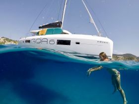A child enjoys swimming in clear waters next to a catamaran, capturing the essence of fun and adventure on a boating trip.