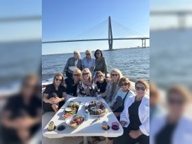 A lively group of friends enjoys a delightful day on the water, sharing food and drinks aboard a pontoon boat with a stunning bridge backdrop.