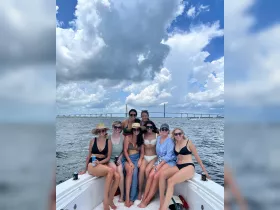 A lively group of friends enjoys a day on the water, posing on the boat with a scenic bridge in the background — perfect for summer celebrations and memorable outings.