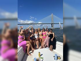 A lively group of friends celebrates on a boat, enjoying the sun and each other's company against the backdrop of a stunning bridge — perfect for bachelorette parties or summer outings.
