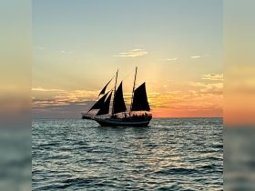 A majestic sailboat with black sails glides across the water at sunset, creating a picturesque scene perfect for romantic evening cruises.