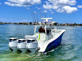 A sleek speedboat with triple Suzuki engines glides through clear waters, showcasing its vibrant design and fishing gear — perfect for adventurous outings.