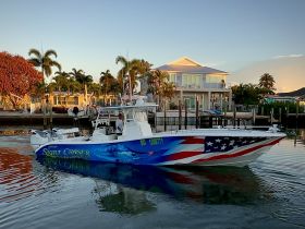 A vibrant speedboat named 'Skirt Chaser' navigates through calm waters, showcasing its striking design and the picturesque waterfront backdrop.