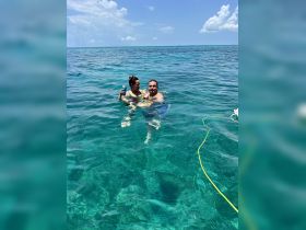 A couple enjoys a refreshing swim in crystal-clear waters, each holding a drink — a perfect moment of relaxation and fun in the sun.