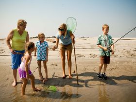 A family enjoys a fun day of fishing on the beach, with children actively participating and learning from adults — a perfect bonding experience in nature.