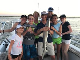 A joyful group of adults and children proudly displays a shark caught during a fishing trip, showcasing a memorable wildlife encounter on the water.