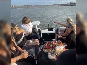 A lively group enjoys a celebration on a pontoon boat, complete with drinks and a beautifully arranged platter of snacks, perfect for a fun day on the water.