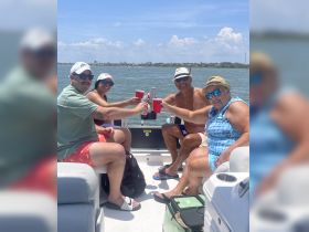 A cheerful group toasts with drinks aboard a pontoon boat, enjoying a sunny day on the water — perfect for celebrations and gatherings.