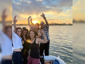 A lively group celebrates at sunset on a boat, raising glasses and enjoying a memorable moment together — perfect for parties and gatherings on the water.