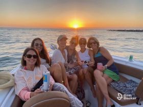 A joyful group of friends enjoys a sunset celebration on a boat, sipping cocktails and capturing memories against a stunning backdrop of the setting sun.