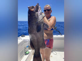 A woman proudly displays her impressive catch while fishing in the ocean, showcasing the thrill of deep-sea fishing adventures.
