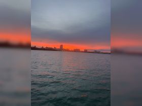 A stunning sunset over the water, with city buildings silhouetted against the vibrant sky — perfect for capturing the serene beauty of evening boat rides.