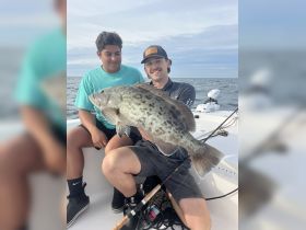 Two friends proudly display their catch while fishing on the open water, showcasing a successful day out at sea.