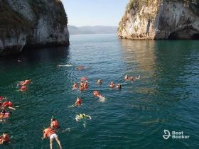 A lively group enjoys swimming and snorkeling in the clear waters near stunning cliffs, showcasing a perfect day of adventure and exploration.