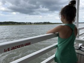 A young girl gazes out over the water from the deck of a boat, enjoying the scenic views — a perfect moment for family outings on the water.