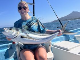 A woman proudly displays her impressive catch while fishing on a boat, showcasing the thrill of a successful day on the water.