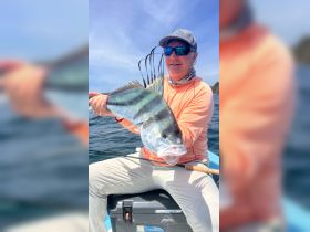 An angler proudly displays his catch while fishing on the ocean, showcasing the thrill of a successful fishing trip.