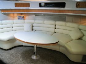 A cozy lounge area inside a boat featuring plush white seating and a central table, perfect for relaxing during a day on the water.