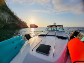 A stunning view of a yacht at sunset, showcasing the boat's sleek design against a picturesque backdrop of rocky cliffs and calm waters.