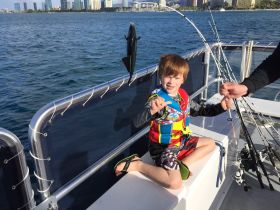 A young boy proudly displays his catch while fishing on a boat, showcasing the joy of family fishing trips in a vibrant setting.