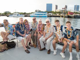A cheerful group of friends and family poses together on a boat, adorned with floral leis, capturing a memorable moment during their aquatic adventure.