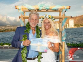 A joyful couple proudly displays their marriage certificate during a beautiful ocean ceremony, capturing a memorable wedding celebration against a stunning backdrop.