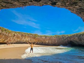 A man stands joyfully in the surf at a stunning beach cave, celebrating the beauty of nature — a perfect spot for adventure seekers and beach lovers.