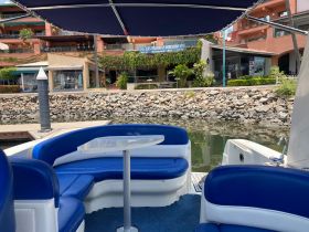 Interior view of a stylish boat with blue seating and a table, perfect for relaxing and enjoying the waterfront scenery.